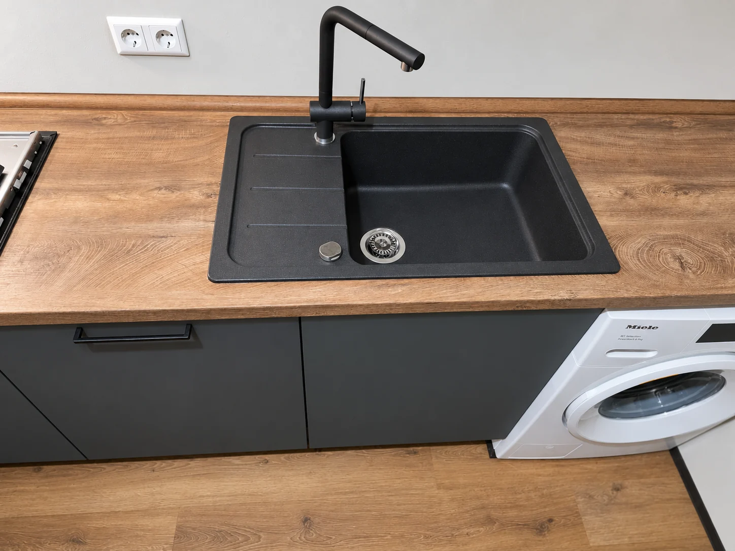 Schwarzes Spülbecken und schwarze Armatur in einer Holzoptik-Arbeitsplatte