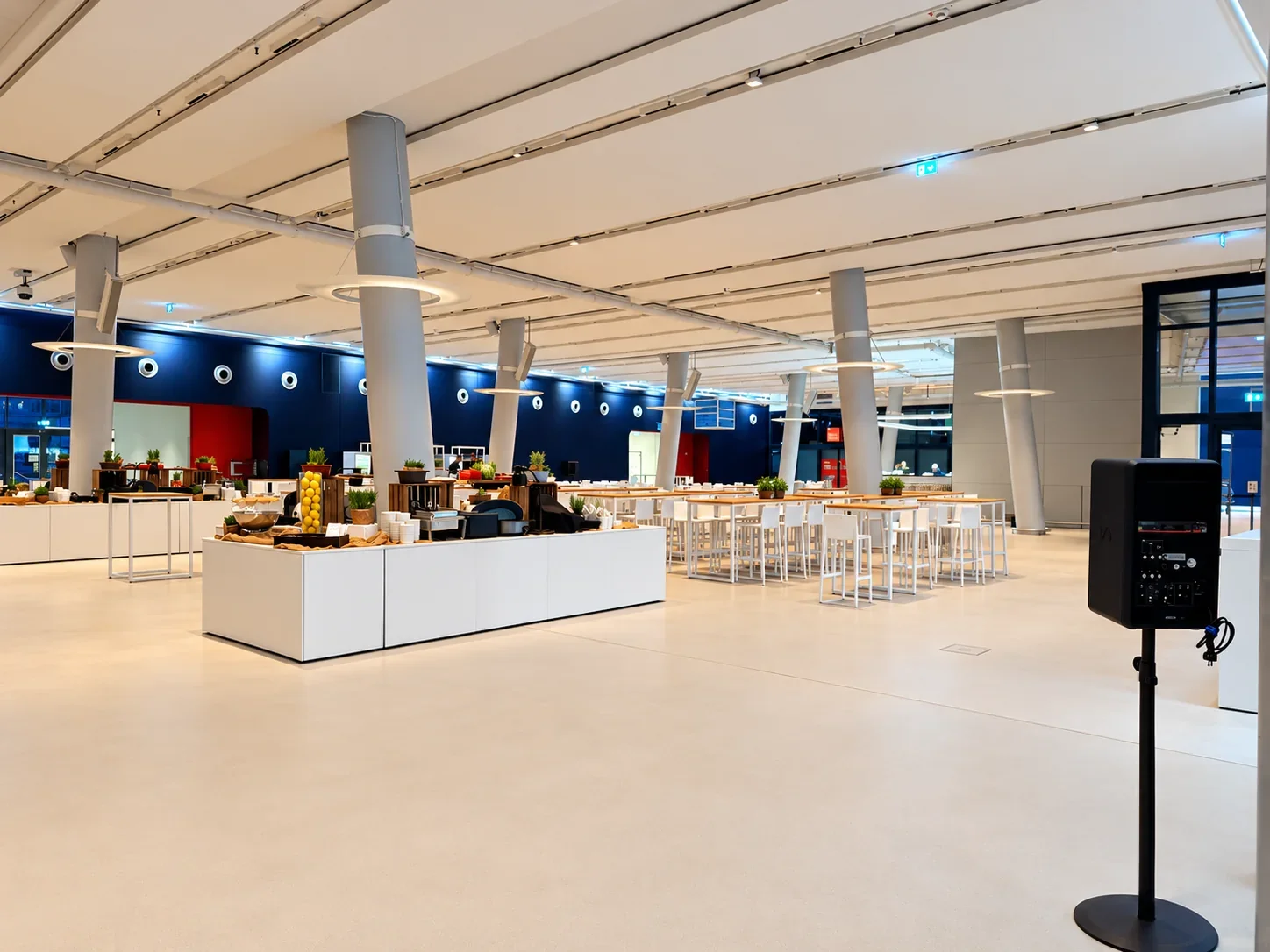 Weite Raumansicht mit weißen Buffetinseln und Hochtischen vor der dunkelblauen Wand im Cruise Center HafenCity