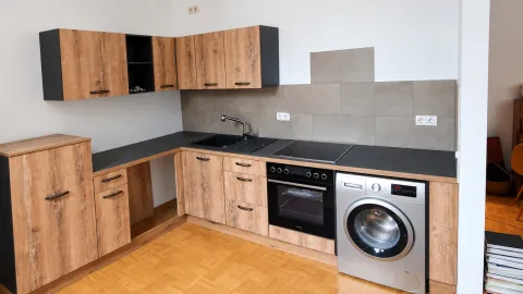 L-förmige Kundenküche mit Holzoptik-Fronten, schwarzen Akzenten, Spüle, Backofen und Waschmaschine